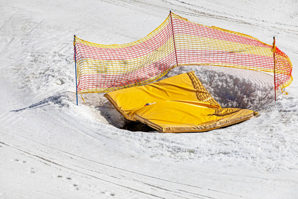 earthen pit covered with a yellow mat fenced with a net on a snowy slope, Safety and Active recreation with the family - Photo, Image