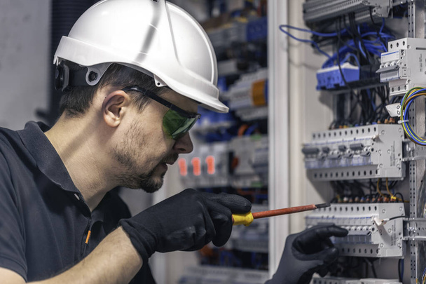 Erkek bir elektrikçi elektrik kablosu kullanarak bir santralde çalışır, ekipmanları aletlere bağlar.. - Fotoğraf, Görsel