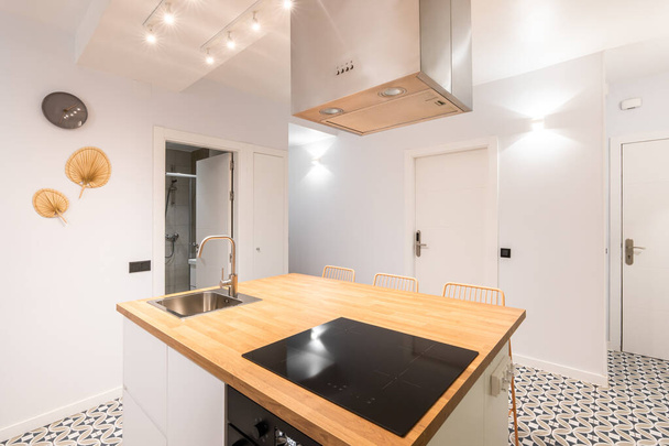 Un tavolo isola in spaziosa cucina monolocale in appartamento moderno con design autori di tendenza. Su una superficie di legno c'è una stufa elettrica a induzione sopra di essa con un sistema di scarico. Mosaico pavimento - Foto, immagini