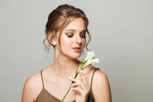 Elegáns nő tökéletes tiszta, friss bőrrel. Boldog női modell természetes smink és fehér tavaszi virág szürke háttér. Kozmetológia, szépség és wellness koncepció - Fotó, kép