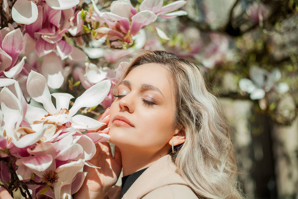 Gyönyörű, fiatal szőke, virágcsokorral. Egy fiatal nő portréja az európai város virágzó magnóliája mellett. Tavasz. - Fotó, kép