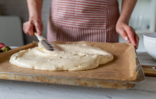 Pâte à tartiner femme avec un grattoir à pâte sur une plaque à pâtisserie. Faire une base de gâteau éponge - Photo, image