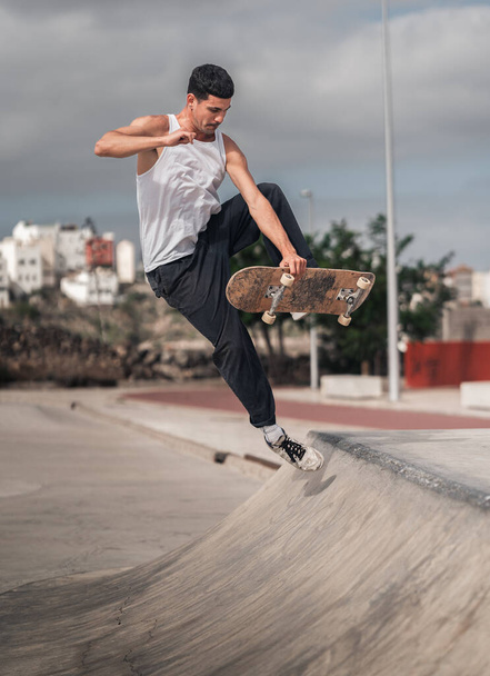 un joven con una camiseta blanca haciendo un truco llamado deshuesado en una rampa de un parque de skate. composición vertical - Foto, imagen