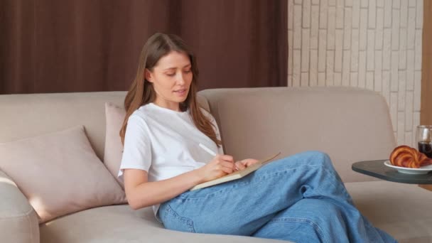 Videó fiatal nő ül a kanapén, és írásban napirend. - Felvétel, videó