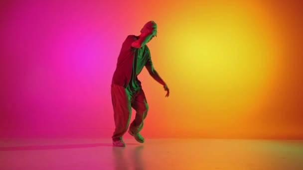 Young man dressed sportswear and dancing in motion in neon light against gradient pink-yellow background. Concept of hobby, sport, creativity, fashion and style, motion, action. Ad - Footage, Video