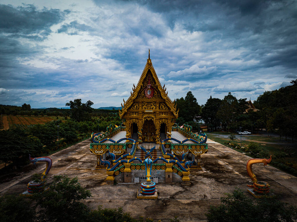 Chachoengsao, Thaimaa, 28. heinäkuuta 2023. Wat Khao Tham Raet, temppeli, jossa on kiviseinä, käärmepatsaiden ympäröimänä. Taivas on pilvetön tummista pilvistä.. - Valokuva, kuva