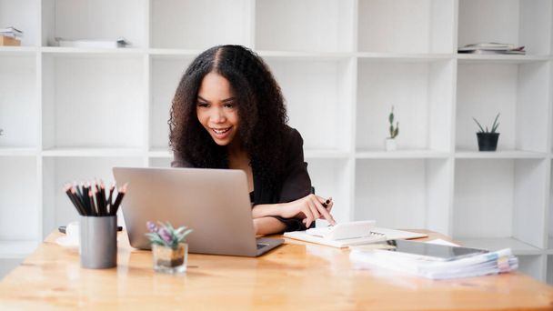 Деловая женщина внимательно работает над своим ноутбуком за современным офисным столом, с документами и кофе поблизости. - Фото, изображение