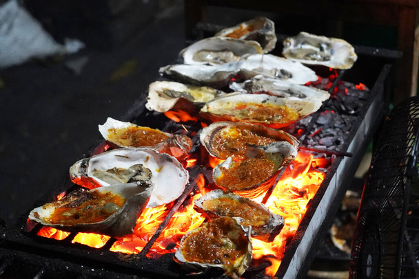 Устрица-гриль в Джакарте, торговец едой. Налегая на гриль, пухлые устрицы предлагают вкус моря с каждым укусом. - Фото, изображение