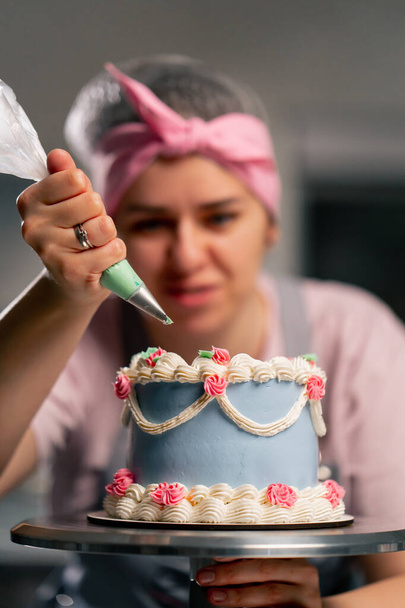 Nahaufnahme einer Bäckerin in einer professionellen Küche, die einen blauen Kuchen mit Sahne dekoriert - Foto, Bild