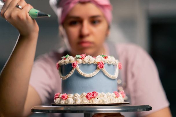 крупным планом женщины-пекаря на профессиональной кухне, украшающей голубой торт кремом - Фото, изображение