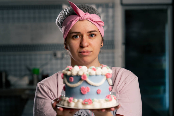 крупным планом на профессиональной кухне женщина-пекарь стоит с готовым тортом в руках - Фото, изображение