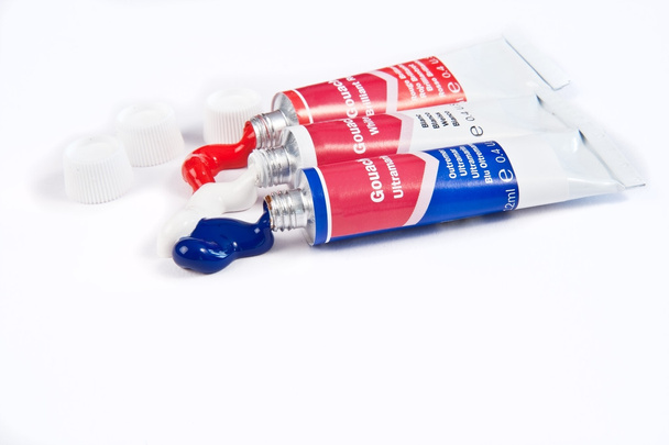 Tubos de tinta acrílica vermelha branca e azul espremidos em papel branco
 - Foto, Imagem