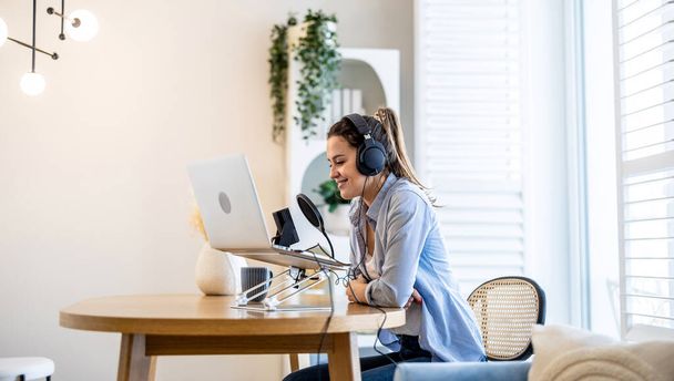 Femme portant des écouteurs assis à un bureau parlant dans le microphone et enregistrant un podcast - Photo, image