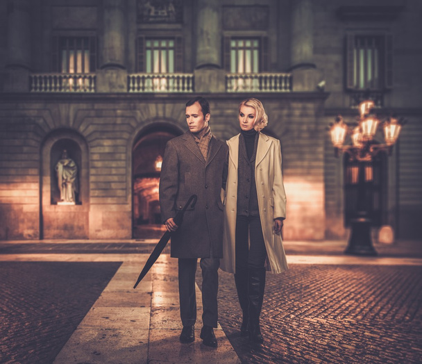 Элегантная пара в пальто против фасада здания вечером
 - Фото, изображение