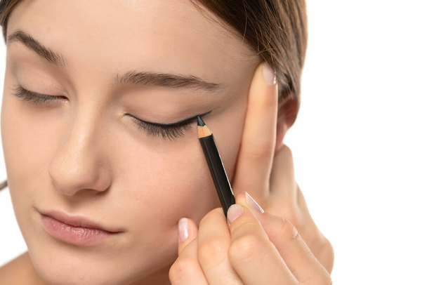 woman applying eyeliner on eyelid with pencil on a white studio background - Photo, Image