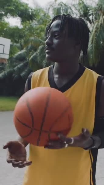 Vertikales Porträt eines schwarzen Sportlers in gelber Aktivkleidung, der nach dem Training auf dem Streetballfeld für die Kamera posiert - Filmmaterial, Video
