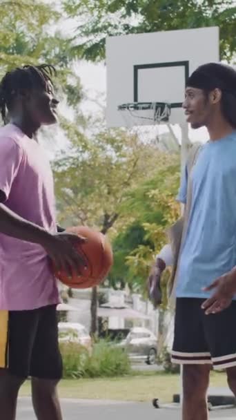 Tiro vertical de dois jogadores de basquete afro-americanos verificando smartphone após jogo ao ar livre - Filmagem, Vídeo