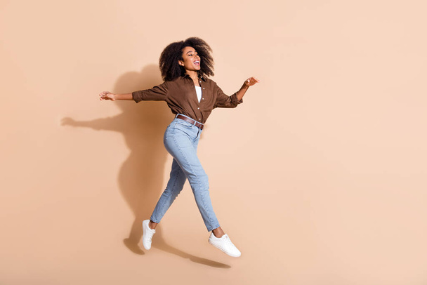 Full size photo of adorable woman dressed brown shirt flying run look at proposition empty space isolated on beige color background. - 写真・画像
