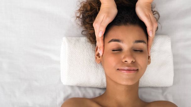 Una mujer afroamericana relajada disfruta de los beneficios relajantes de un masaje de cabeza profesional en un ambiente de spa - Foto, Imagen