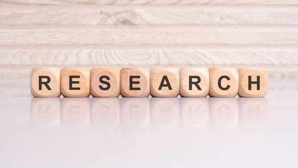 wooden cubes displaying the word 'RESEARCH' arranged on a glossy gray surface, with a reflection and wooden background - Photo, Image