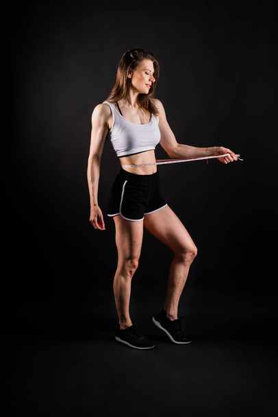 ダークイエローの背景にダイエット後の測定テープで腰を測定する運動スリム女性 - 写真・画像