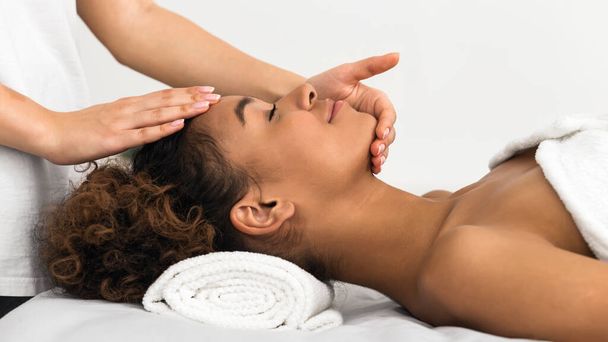 Un terapeuta experto ofrece un relajante masaje de spa enfocado en una cara de damas afroamericanas - Foto, imagen