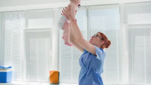 iloinen lääketieteellinen työntekijä oksentaa pienen lapsen leikkiessään hänen kanssaan lääkärin toimistossa - Materiaali, video