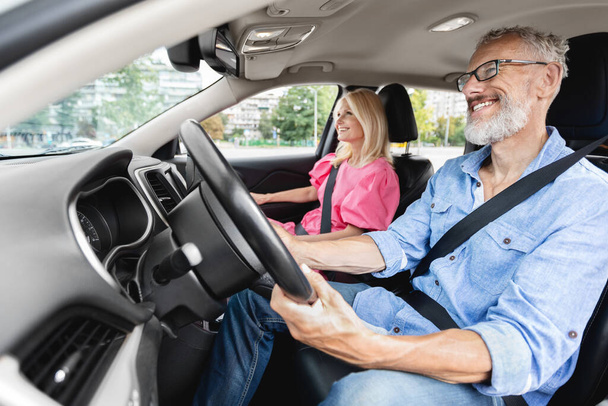Старшая супружеская пара на выходе на пенсию в машине во время дневной поездки, со стариком, сосредоточенным на дороге, и женщиной-пассажиром, смотрящей на - Фото, изображение