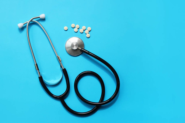 Stethoscoop en witte pillen op een blauwe achtergrond, bovenaanzicht. Cardiologie en gezondheidszorg. Auscultatie apparaat. Medisch zorgconcept. Medisch instrument. Apparatuur voor uscultatie - Foto, afbeelding