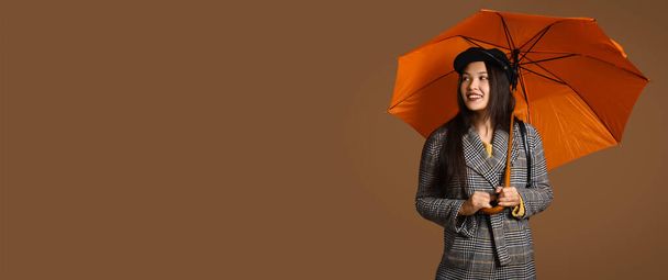Krásná mladá asijská žena s deštníkem na hnědém pozadí s prostorem pro text - Fotografie, Obrázek