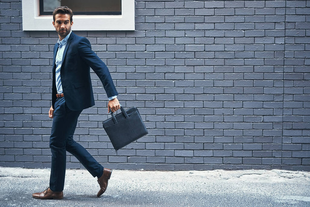 Man, walking and brick wall in city for business with briefcase, work commute, and corporate company. Male executive, bag and urban background for banking career with travel, professional and street. - Photo, Image