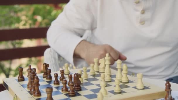Közelkép két középkorú névtelen férfi kezéről, akik a szabadban ülnek a nyári napon, sakkoznak a fedélzeten, mozgatják és elfogják az ellenfelek darabjait. - Felvétel, videó