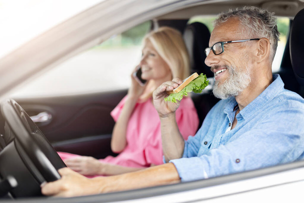 Egy idős, nyugdíjas házaspár egy friss salátás szendvicsen osztozik, élvezve az autójuk kényelmét, elősegítve az egészséges étkezési szokásokat az idősek körében. - Fotó, kép