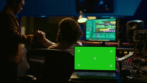 Artist and sound designer working as a team to produce new tracks, greenscreen laptop. Musician and audio technician collaborating on music, mixing on audio console with motorized faders. Camera B. - Photo, Image