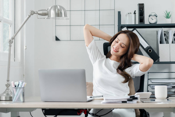 Расслабленная профессиональная женщина берет перерыв, чтобы растянуться на рабочем месте, сигнализируя момент заслуженного отдыха в ее напряженный день. - Фото, изображение