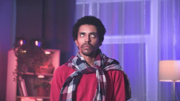 задумчивый молодой черный мужчина смотрит вокруг, думая о событиях, стоя в уютной комнате - Кадры, видео