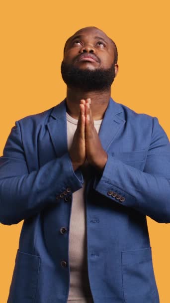 Vertikální video Pious Afroameričan se modlí ke svému bohu, prosí o odpuštění. Duchovní BIPOC muž dělá uctívání rukou gesto, přiznání, prosí o odpuštění, izolované přes studio pozadí - Záběry, video