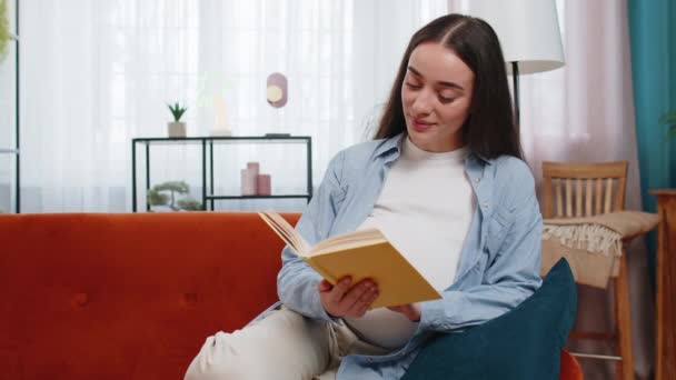 Pregnant Caucasian woman lady reading book feeling relax on cozy sofa couch at home. Future mother beautiful female read advice child care guide prepare prenatal. Relaxation and pregnancy concept. - Footage, Video