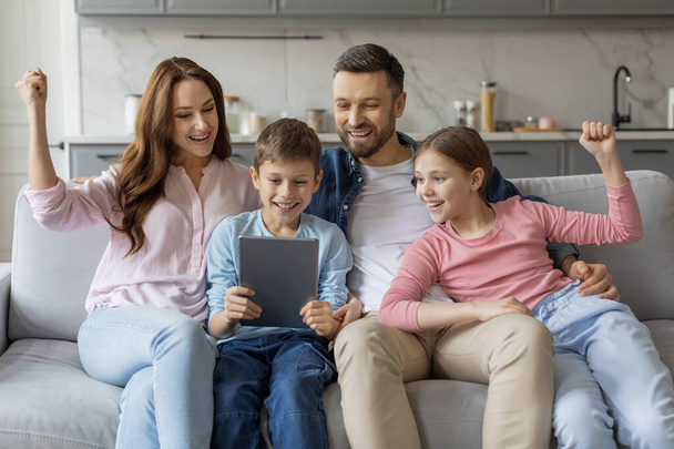 Tento obrázek ukazuje radostnou evropskou rodinu sdílející tablet, objímající lásku a náklonnost v pohodlí svého domova - Fotografie, Obrázek