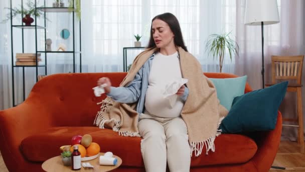 Donna caucasica malsana incinta avvolta in una coperta che soffia il naso nel tessuto mentre seduta sul divano in soggiorno. Malata futura mamma stanca della congestione nasale e dei sintomi del raffreddore a casa. - Filmati, video
