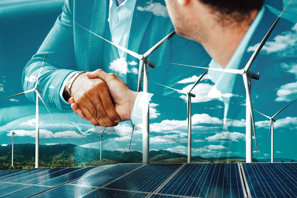 Double exposure graphic of business people handshake over wind turbine farm and green renewable energy worker interface. Concept of sustainability development by alternative energy. uds - Photo, Image