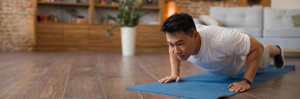 Strong asian mature man making strength workout, doing push ups on sports mat, having domestic workout. Sporty korean male training his body, leading active lifestyle, panorama with copy space - Photo, Image
