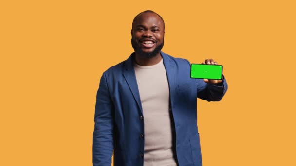 Excited african american man holding isolated screen phone, doing recommendation. Joyous person presenting mockup smartphone, showing positive feedback, isolated over studio background, camera B - Footage, Video