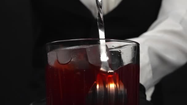 Macrografie, observeer de vaardige handen van een vrouwelijke barman die vakkundig rode siroop in glas giet met ijs op zwarte achtergrond. Elk close-up shot van een vrouw bereidt rode cocktail in glas. Bestanddelen. - Video