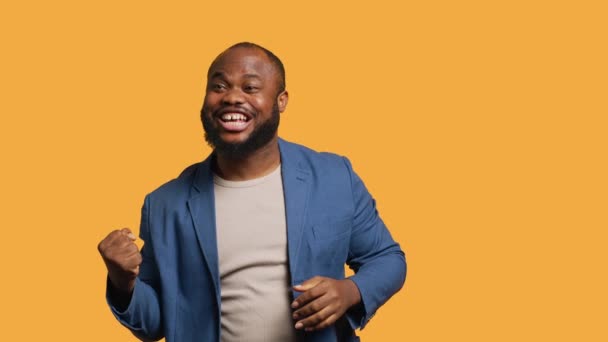 Portret van een vrolijke Afro-Amerikaanse man die feest viert, met positieve emoties. Delighted BIPOC persoon enthousiast over prestatie, juichen en gebaren, studio achtergrond, camera A - Video