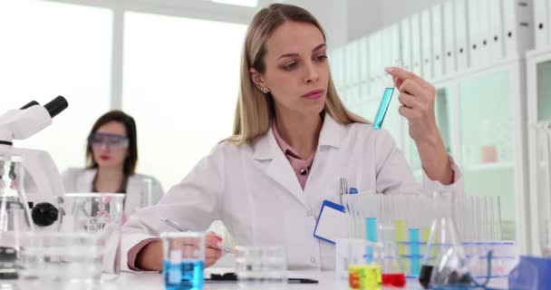 女性は液体を含む試験管での反応の観察を記録する. 科学者はまだ科学プロセスの遅い動きに完全に集中しています - 映像、動画