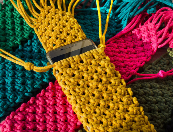 Petits sacs tricotés à l'aide de la technique de macramé à partir de cordon de coton. Sacs multicolores pour téléphones mobiles sur un fond en bois. - Photo, image