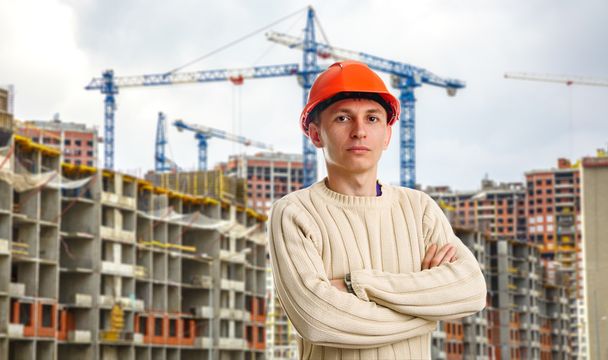 Obrero en casco rojo sobre fondo de edificios
  - Foto, Imagen