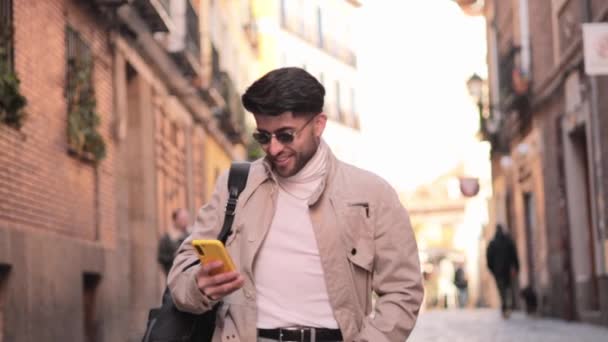 Vidám modern férfi sétál a város utcájában, és használja az okostelefonját. Kolumbiai férfi. - Igen. Kiváló minőségű FullHD felvételek - Felvétel, videó
