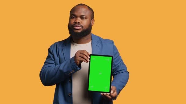 Πορτρέτο της Αφρικής Αμερικανός άνθρωπος κάνει μάρκετινγκ επιρροή χρησιμοποιώντας πράσινη οθόνη tablet, φόντο στούντιο. Χαμογελώντας BIPOC πρόσωπο που κρατά κενό αντίγραφο χώρο mockup συσκευή, κάμερα Α - Πλάνα, βίντεο